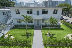 Miami Beach apartment for rent - a white house with a lawn and palm trees in front