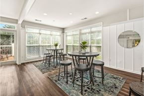 Owings Mills apartment for rent - A room with white walls, floor-to-ceiling windows, and medium-brown wood floors. There are two small square rugs, each with a round pub table and four chairs on top.