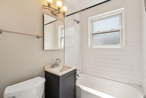 Denver apartment for rent - A white bathroom with a tub, sink, and mirror.