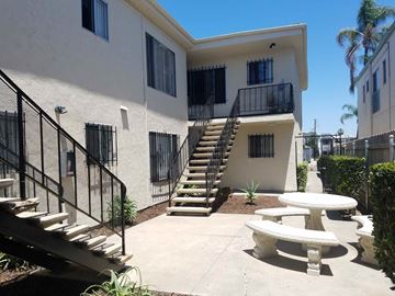 San Diego apartment for rent - A white building with a black railing and a staircase leading to the second floor.