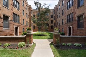 Chicago apartment for rent - a walkway between two brick buildings with grass and flowers
