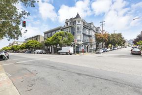 San Francisco apartment for rent - A street view with a large building on the corner and cars parked on the side of the road.