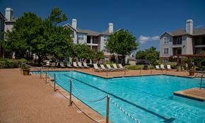 Oklahoma City apartment for rent - A pool surrounded by chairs and trees with apartment buildings in the background.