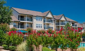 Edmond apartment for rent - A building with a pool and red flowers in front.