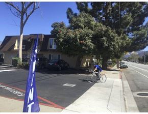 San Luis Obispo apartment for rent - A person riding a bicycle on a street with a blue flag on the left.