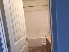 Sidney apartment for rent - A white door with a gold handle is open to a bathroom with a toilet and a bathtub.