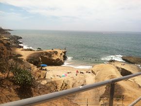 San Diego apartment for rent - A beach with people swimming and a railing in the foreground.