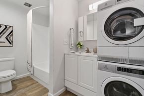 Burien apartment for rent - A white washing machine sits in a laundry room next to a toilet.