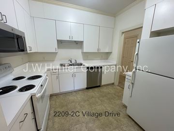 Wilson apartment for rent - A kitchen with white cabinets and appliances, including a stove and refrigerator, with a sign that reads "J.W. Hunter Company, Inc." and an address of "2209-2C Village Drive