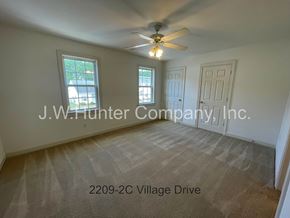 Wilson apartment for rent - A room with a carpet floor, a ceiling fan, and a window showing a view of trees and a building.
