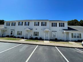 Wilson apartment for rent - A white building with multiple windows and doors is situated in a parking lot.