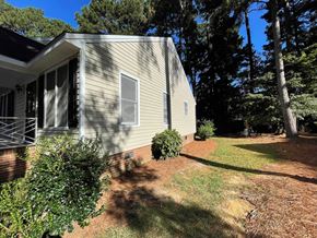 Wilson apartment for rent - A house with a grey siding and a brown roof is surrounded by trees and bushes.