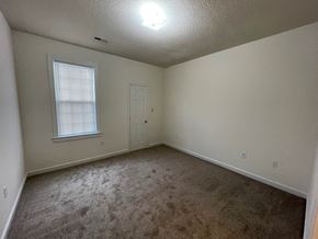 Wilson apartment for rent - A room with a carpeted floor, a window with blinds, and a door.