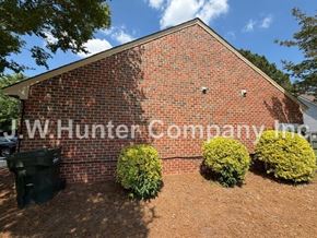 Wilson apartment for rent - A red brick building with a black dumpster in front and three green bushes on the side.
