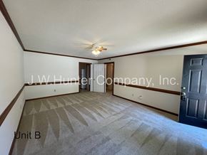 Wilson apartment for rent - A carpeted room with a ceiling fan and a door at the end.