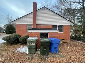 Wilson house for rent - A small house with a red brick chimney and two trash bins in front.