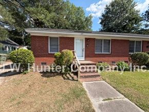 Wilson apartment for rent - A red brick house with a white door and windows, surrounded by greenery and a concrete pathway leading to the front door.