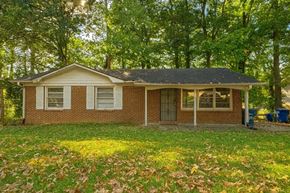 Atlanta house for rent - A small house with a brown brick exterior and a grey roof surrounded by trees.