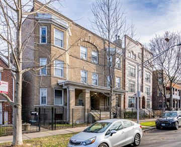 Chicago apartment for rent - A silver car is parked in front of a brown building with a black fence.