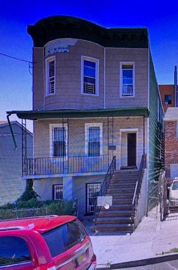 The Bronx apartment for rent - A red car is parked in front of a two-story building.