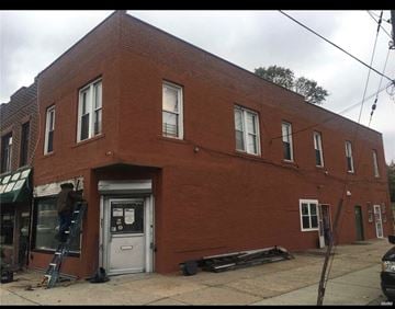 Queens apartment for rent - A man is on a ladder painting the front of a red brick building.