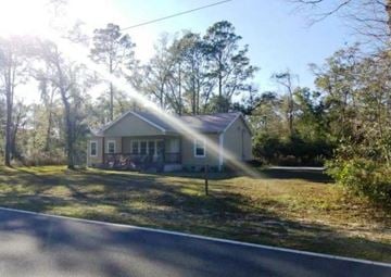Crawfordville house for rent - A house with a white roof and a porch is surrounded by trees.