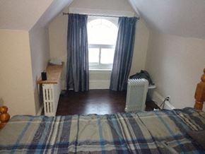 Ottawa apartment for rent - A bedroom with a bed, a radiator, and a window with curtains.
