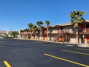 Bullhead City apartment for rent - A parking lot with a building and palm trees in the background.