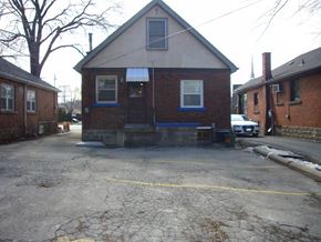 Hamilton apartment for rent - A small brick building with a porch and a car parked in front.