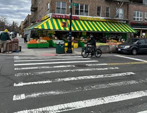 Astoria apartment for rent - A man on a motorcycle is crossing the street in front of a produce stand.