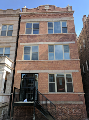Chicago apartment for rent - A brick building with a balcony and a window with a reflection of a person.