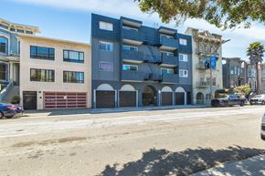San Francisco apartment for rent - A street view of a multi-story building with a blue facade and a car parked in front.