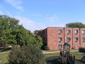 Carol Stream apartment for rent - A playground with a slide and a green roof is in front of a red brick building.