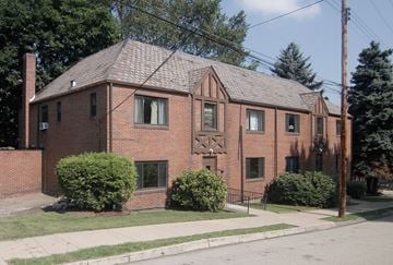 Pittsburgh apartment for rent - A red brick house with a black fence and green bushes in front.