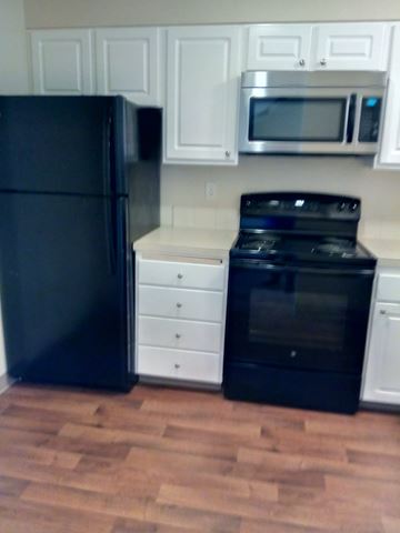 Portland apartment for rent - A black refrigerator is in a kitchen with white cabinets.