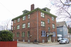 Pittsburgh apartment for rent - A red brick building with green trim and a grey car parked in front.
