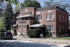 Swissvale apartment for rent - A red brick house with a porch and a car parked in front.