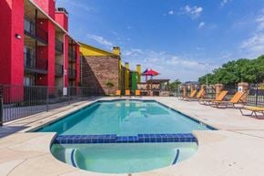 Dallas apartment for rent - A swimming pool surrounded by a red building and lounge chairs.