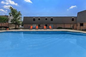 Fort Worth apartment for rent - A swimming pool with orange chairs and a building in the background.