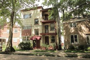 Pittsburgh apartment for rent - A building with a balcony and a red awning is surrounded by trees and bushes.