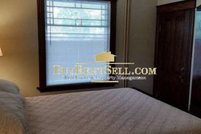 Minneapolis apartment for rent - A bedroom with a bed in the foreground and a window with a sign that says BuyKentSell.com Real Estate & Property Management.