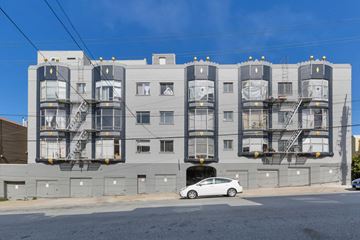 San Francisco apartment for rent - A white car is parked in front of a grey building with a fire escape.