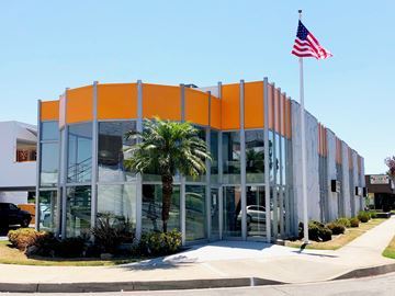 Downey apartment for rent - A modern building with a palm tree in front and an American flag on top.