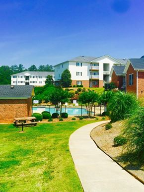 Easley apartment for rent - A grassy area with a bench and a pool in front of apartment buildings.
