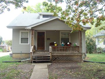 Lawrence apartment for rent - A small house with a porch and a hose on the ground.