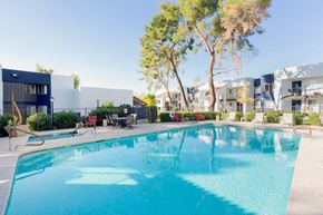 Phoenix apartment for rent - A swimming pool in front of a building with trees and chairs around it.