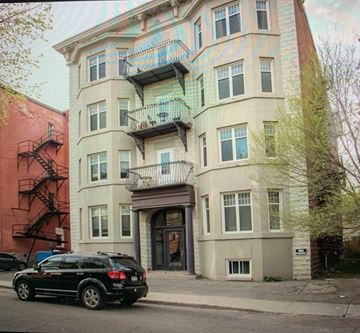 Ottawa apartment for rent - A black SUV is parked on the sidewalk in front of a two-story building with a balcony.