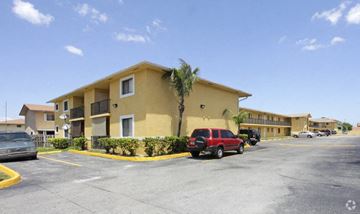 Hialeah apartment for rent - A red car is parked in a parking lot in front of a yellow building.