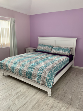 Maywood apartment for rent - A bed with a white headboard and a blue and white patterned comforter sits in a room with purple walls.