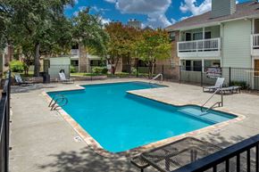 San Antonio apartment for rent - A swimming pool surrounded by a fence and trees.